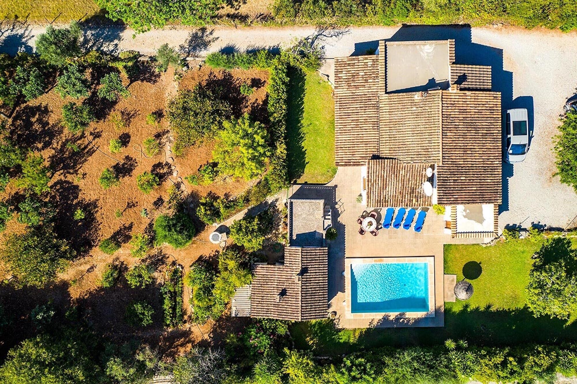 An aerial view of a house with a swimming pool, a patio with lounge chairs, and a vehicle parked nearby.