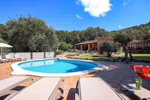 A swimming pool with lounge chairs, a patio area, and a building with a tiled roof.