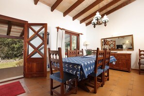 A dining area with a wooden table and chairs, a chandelier, and a large window with curtains.