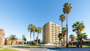 Un hotel de varios pisos con diseño moderno, situado en una esquina con palmeras y cielo despejado.