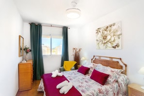 A hotel room with a bed, a chair, a dresser, a window with curtains, and a painting on the wall.