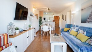Una sala de estar moderna con sofá, televisión, mesa de comedor y cocina al fondo.
