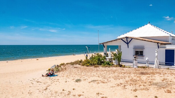 Un edificio frente a la playa con fachada blanca, puerta azul y un pequeño porche.