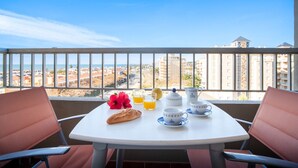 Un balcón con una mesa dispuesta para el desayuno, que incluye pan, fruta y tazas.