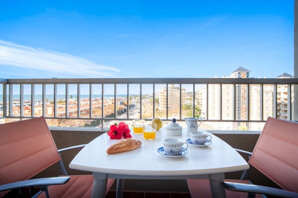 Un balcon avec une table préparée pour le petit-déjeuner, comprenant du pain, des fruits et des tasses.