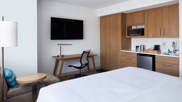 A hotel room with a bed, a desk with a chair, a television, wooden cabinets, a microwave, and a dishwasher.