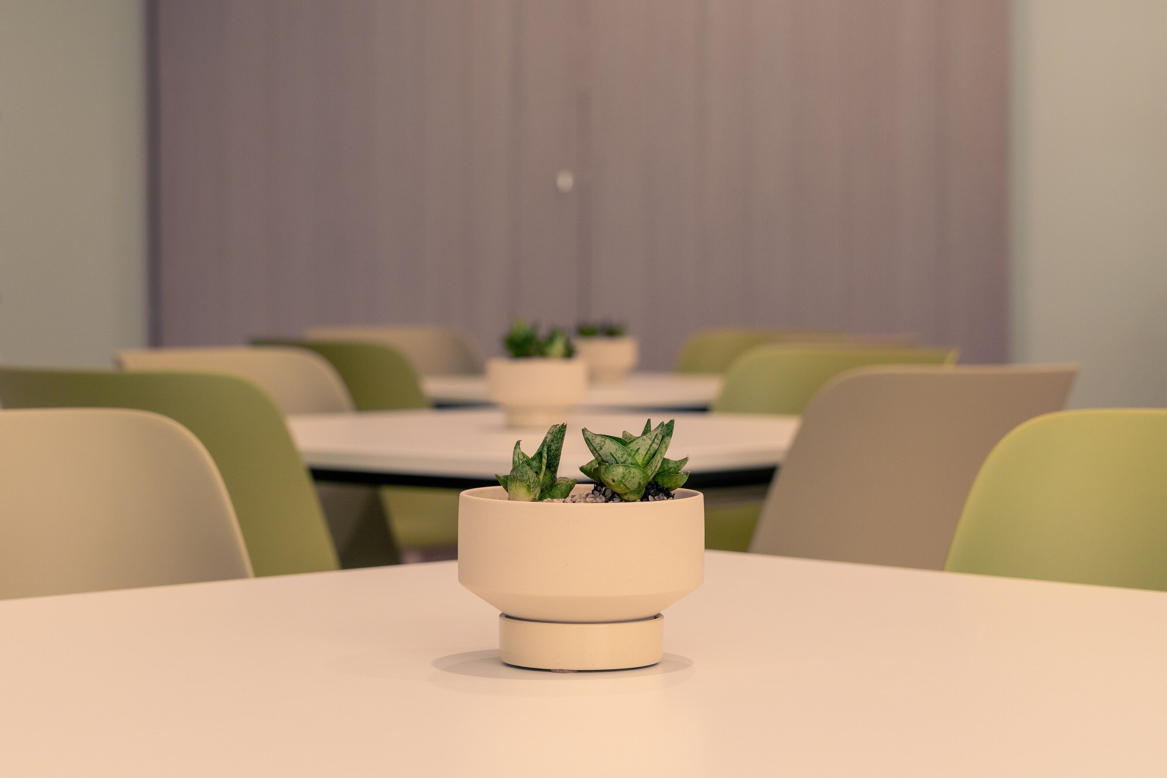 A modern meeting room with white tables and green chairs.