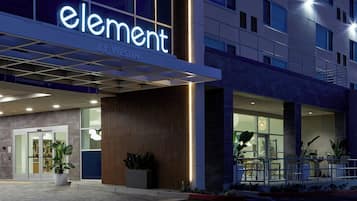 Entrada de hotel con diseño moderno, destacando un letrero grande de 'element by westin', puerta de cristal y plantas en macetas.