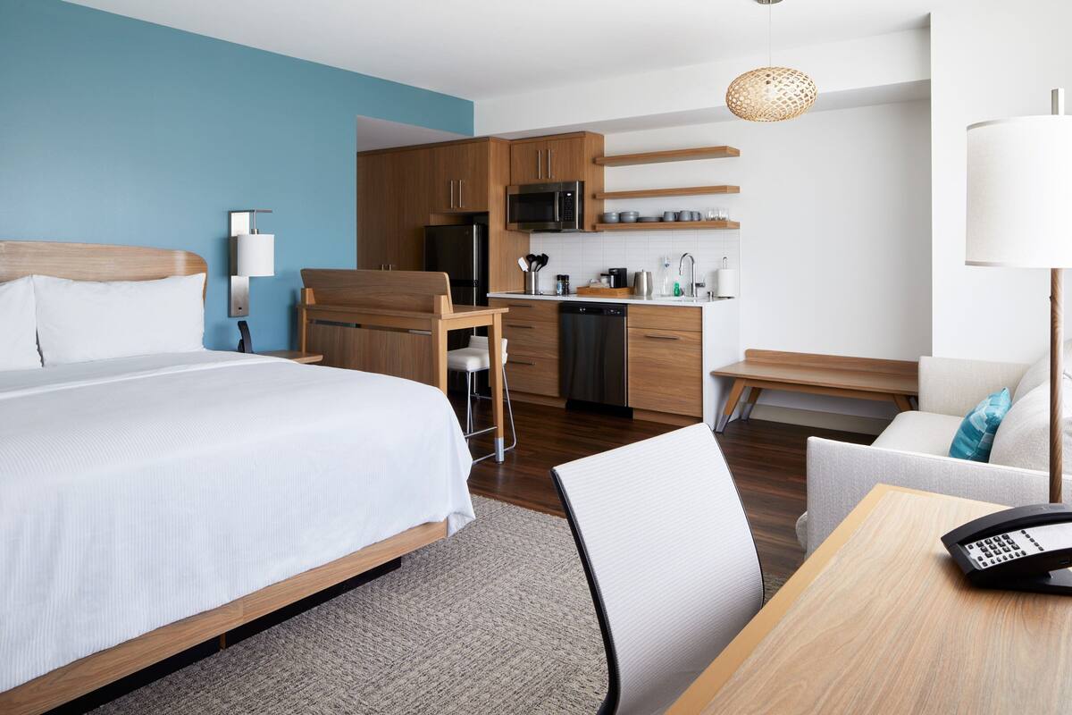 Ein Hotelzimmer mit Bett, Schreibtisch mit Telefon, einer Küchenzeile und einer Sitzecke.
