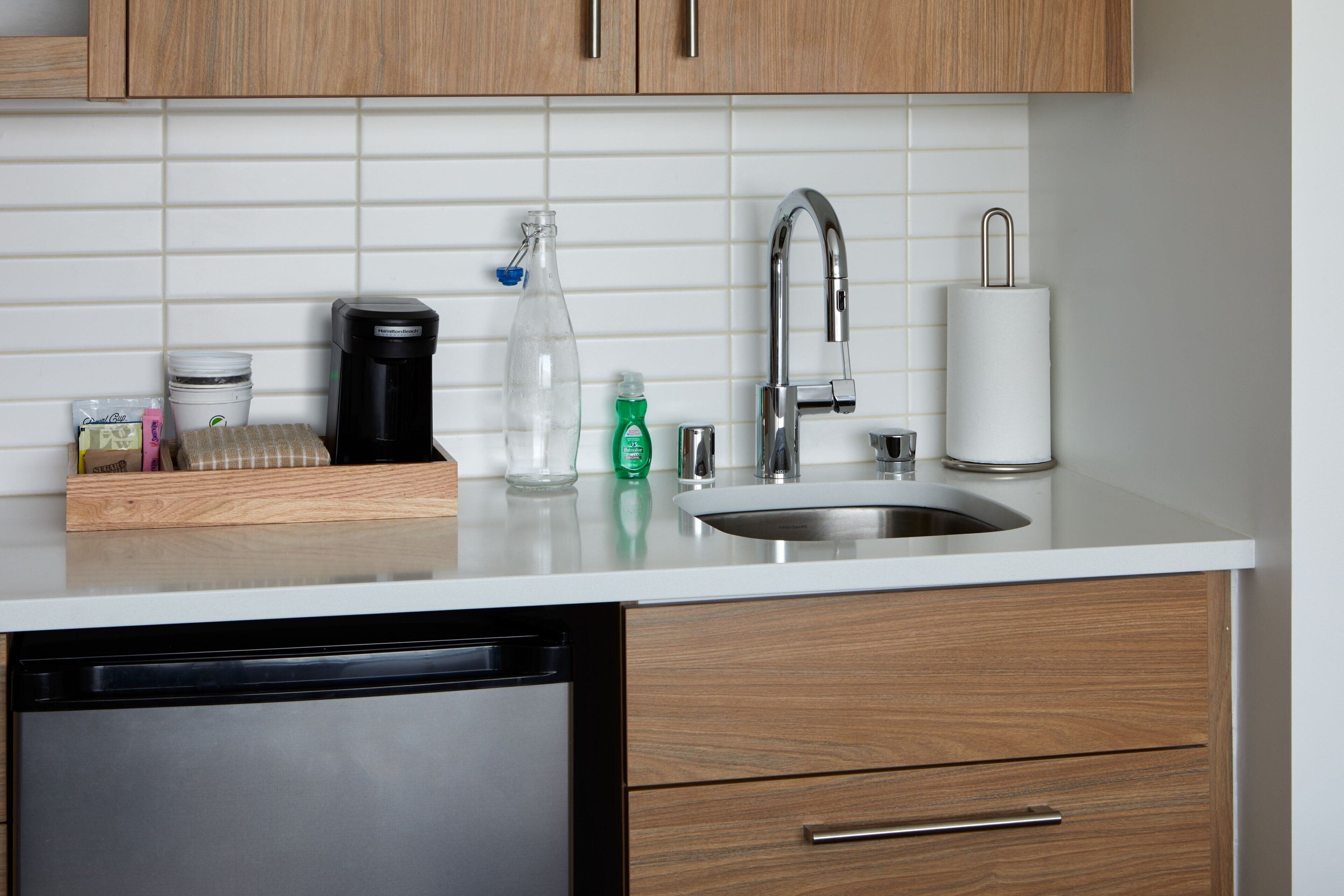 A kitchen with a dishwasher, wooden cabinets, a white countertop, a stainless steel sink, and a coffee maker.