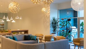 Ein modernes Interieur mit einer gebogenen Couch, mehreren Sesseln, hängenden, kugelförmigen Leuchten und einem an der Wand befestigten Fahrrad.