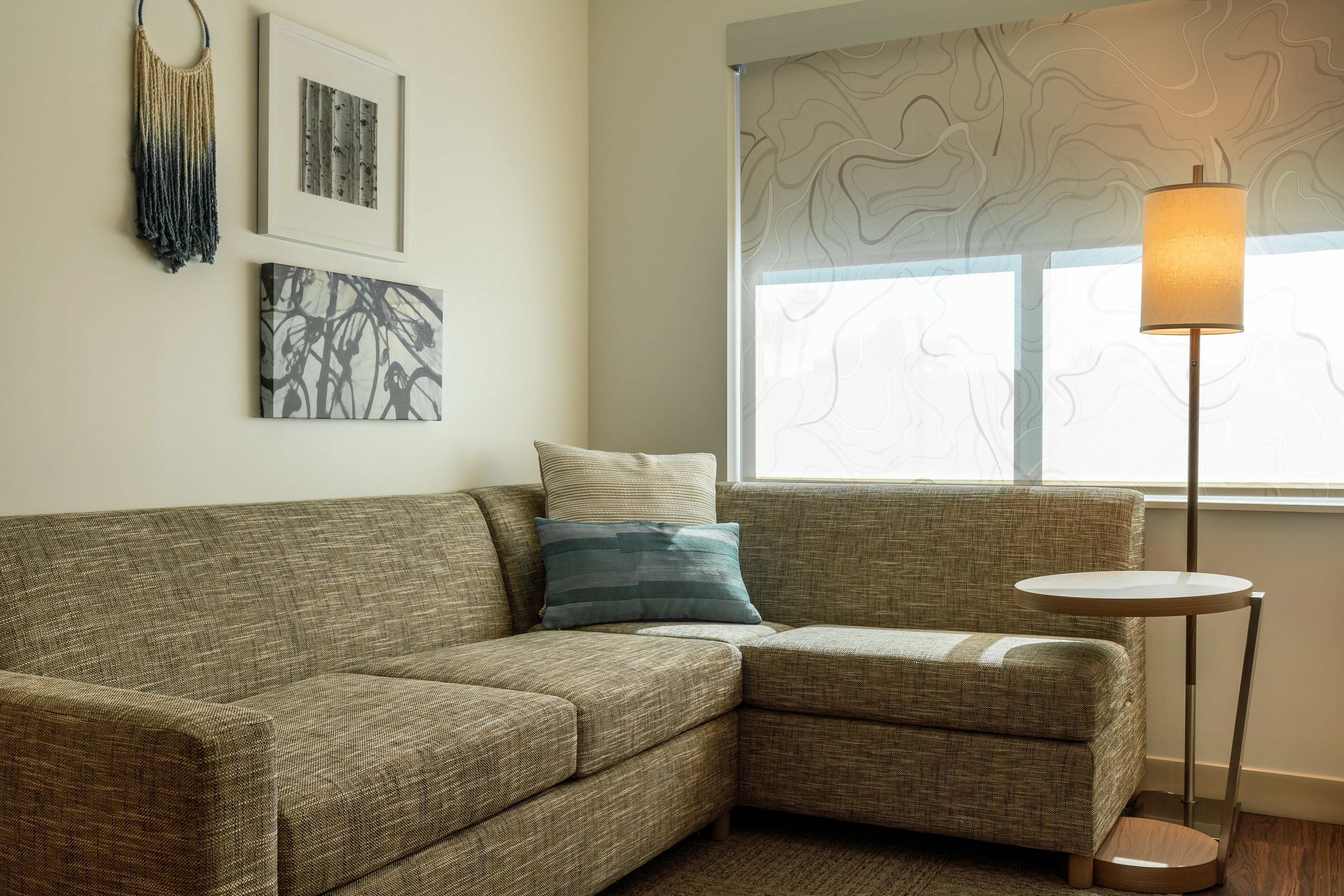 A corner sofa with a cushion, a small round table, and a floor lamp.