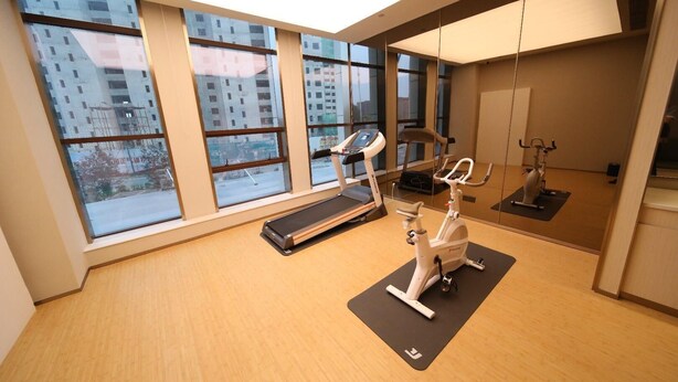 Ein Fitnessstudio mit Trainingsgeräten, Laufband und großen Fenstern mit Blick auf die Stadt.