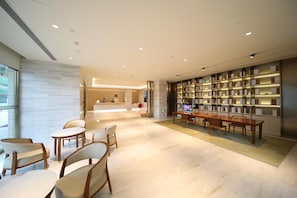 A modern hotel lobby with a reception desk, seating area, and a large bookshelf. - Ji Hotel (Changchun)