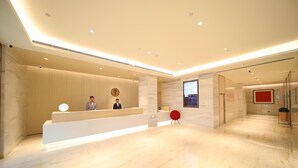 Ein moderner Hotel-Empfangsbereich mit Marmorboden, einer Rezeption, einem digitalen Bildschirm und einem roten Sessel.