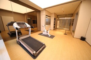 Un gimnasio con cinta de correr, bicicleta estática y colchonetas de ejercicio.
