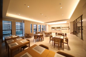 A modern dining area with tables and chairs, large windows, and a kitchen in the background. - Ji Hotel (Changchun)