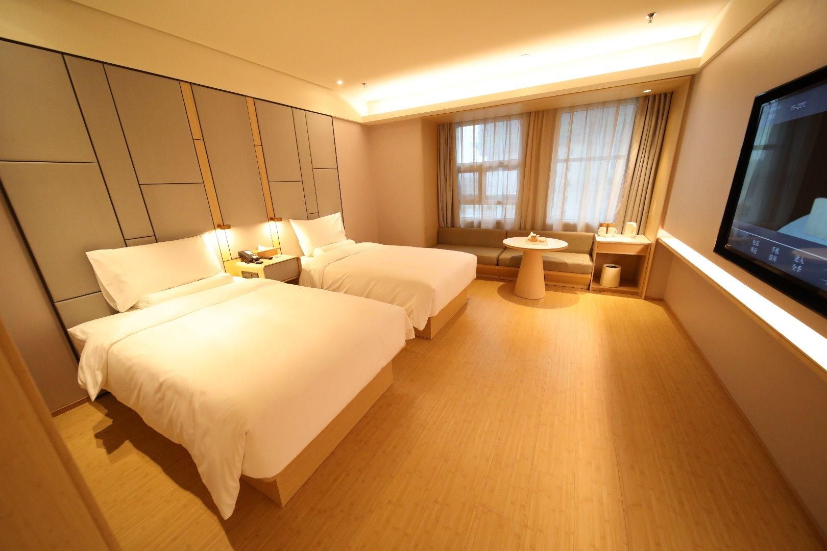 A hotel room with two beds, a sofa, a small table, and a TV.