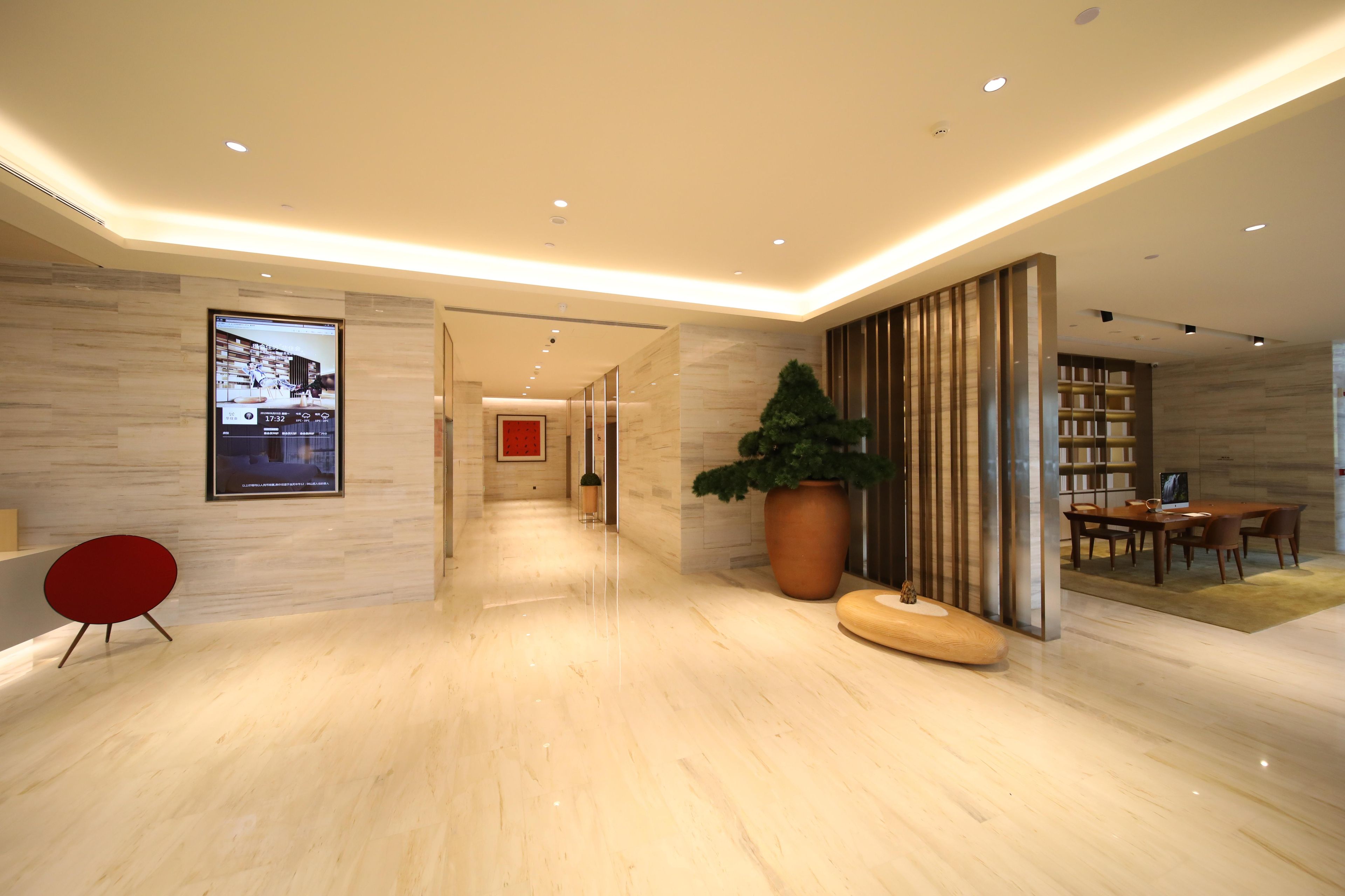 Un moderno vestíbulo de hotel con piso de mármol, una silla roja, una planta grande en maceta, un banco de madera y un comedor con mesas y sillas.