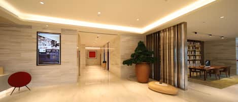 Un moderno vestíbulo de hotel con piso de mármol, una silla roja, una planta grande en maceta, un banco de madera y un comedor con mesas y sillas.