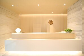 Una recepción con un panel de pared de madera, un letrero circular con caracteres chinos y una planta en maceta.