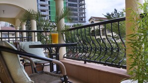 Un balcón con una silla de mimbre, una planta en maceta y un vaso de jugo de naranja.