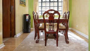Un comedor con una mesa y sillas de madera, un refrigerador y un ventanal con cortinas.