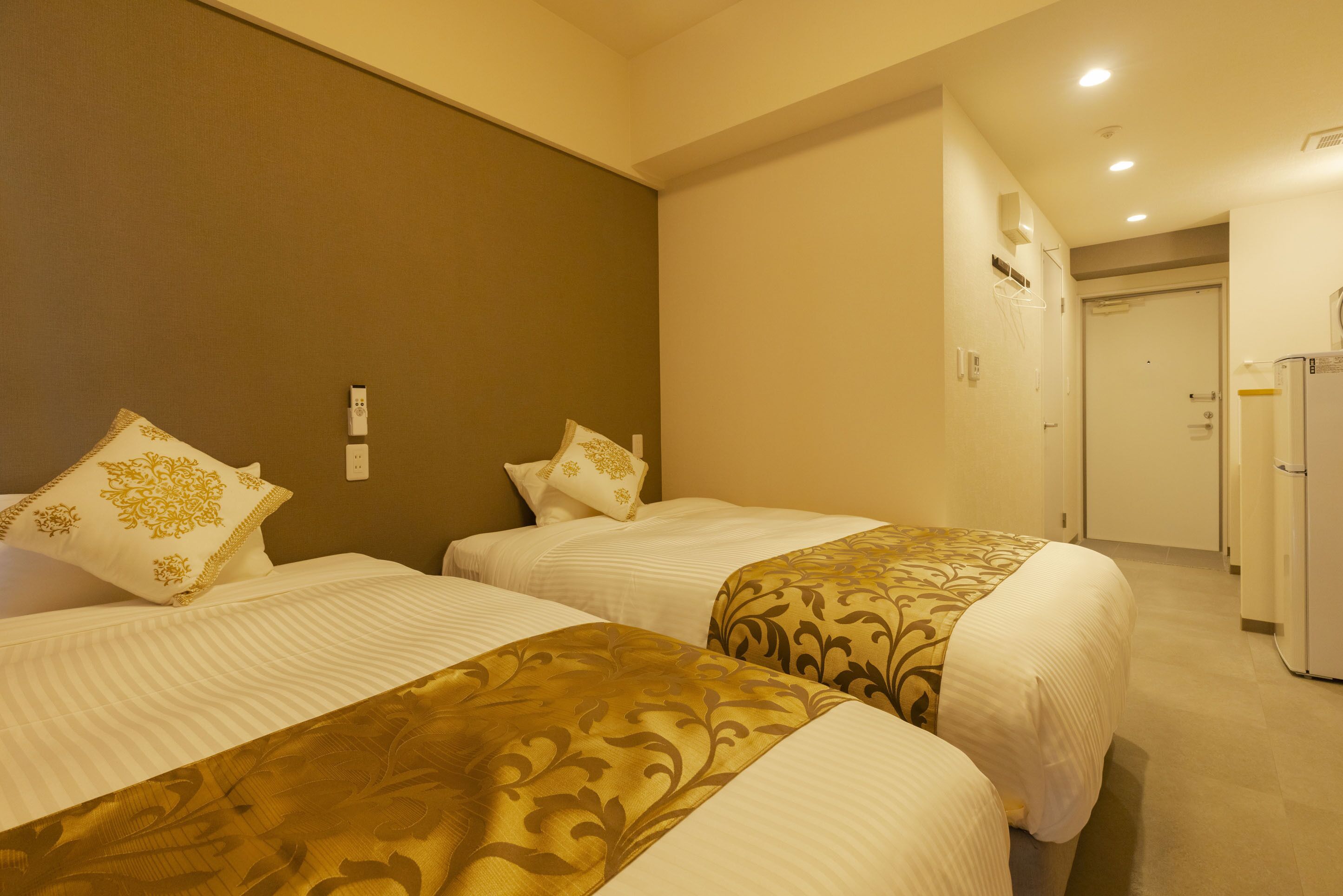 Ein Hotelzimmer mit zwei Betten, jedes mit einer gemusterten Tagesdecke und passenden Kissen. Das Zimmer hat eine neutrale Farbgestaltung und eine Tür zu einem Flur.