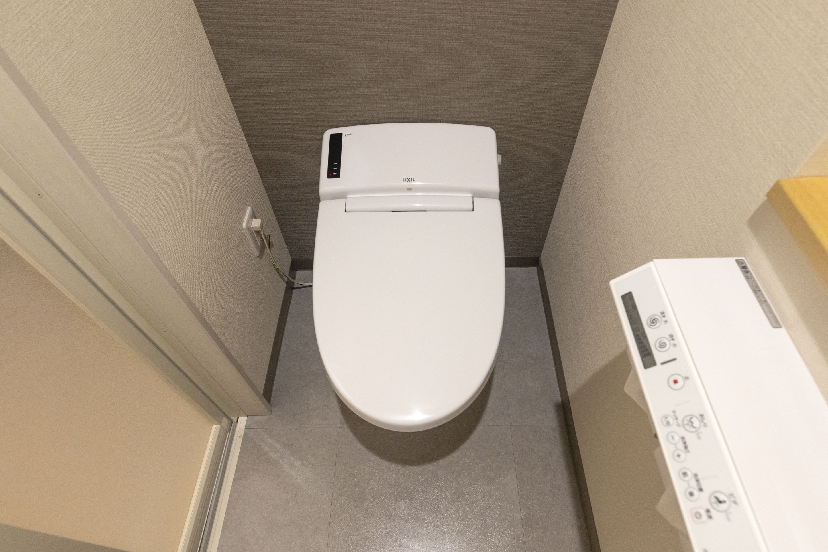 A white toilet in a small bathroom with a control panel on the right.