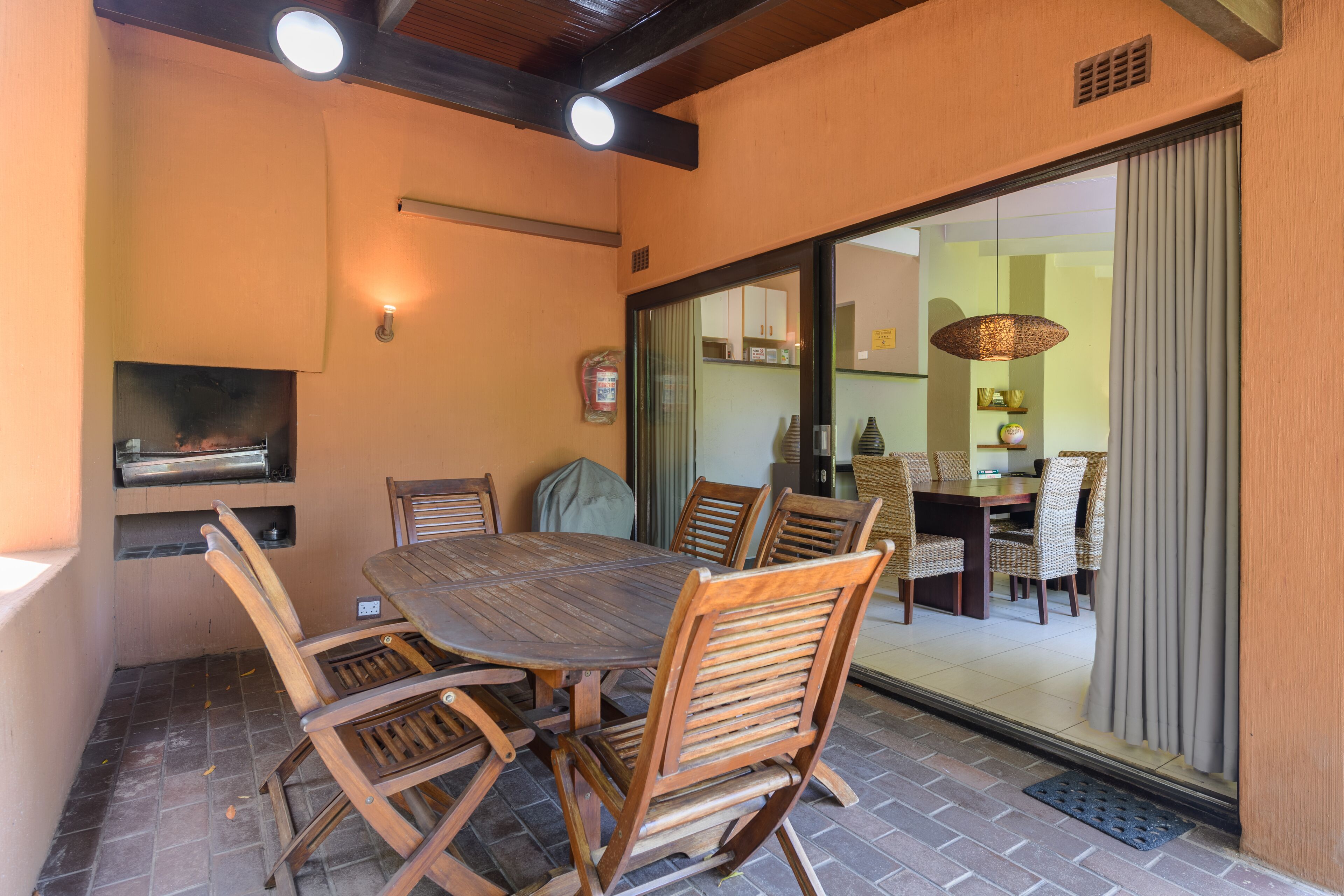 A patio with a wooden table and chairs, a grill, and a sliding glass door leading to an indoor dining area.