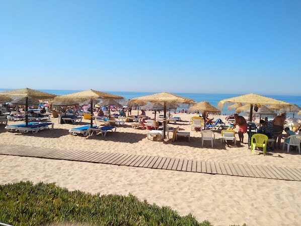 Uma praia com espreguiçadeiras, guarda-sóis e uma passarela de madeira que dá para a água.