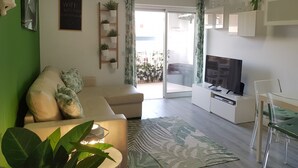 En moderne stue med sofa, fjernsyn og en balkon med planter.