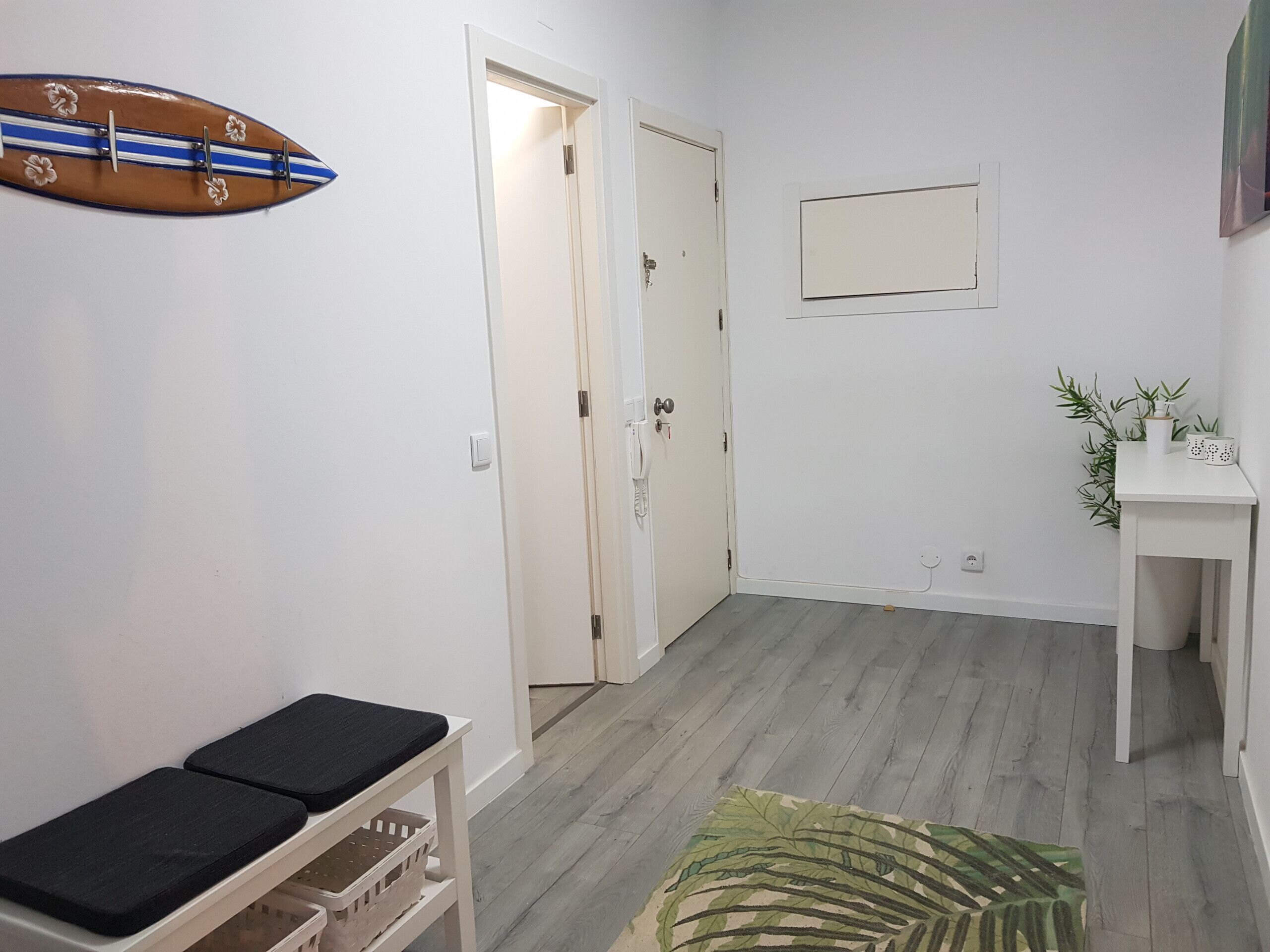 A hallway with a bench, a surfboard decoration, a door, a small table with plants, and a mirror on the wall.