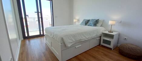 Ein Schlafzimmer mit einem Bett, Nachttischen, einer Lampe, einer Schiebeglastür und Holzboden.