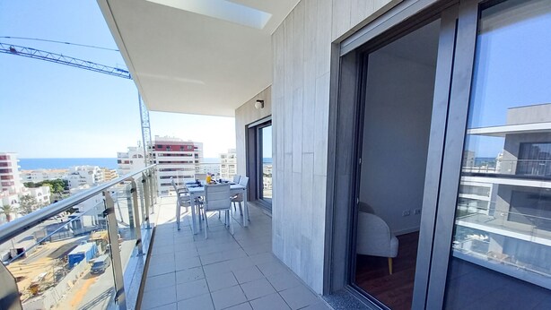 A balcony with a table and chairs, a sliding glass door, and a view of the cityscape and sea. - Alto Forte Novo 4, Vista Mar, Ar Condicionado e Garagem (Quarteira)