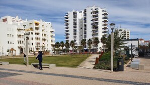 A modern urban plaza with a central grassy area, paved walkways, and high-rise residential buildings in the background. - Alto Forte Novo 4, Vista Mar, Ar Condicionado e Garagem (Quarteira)