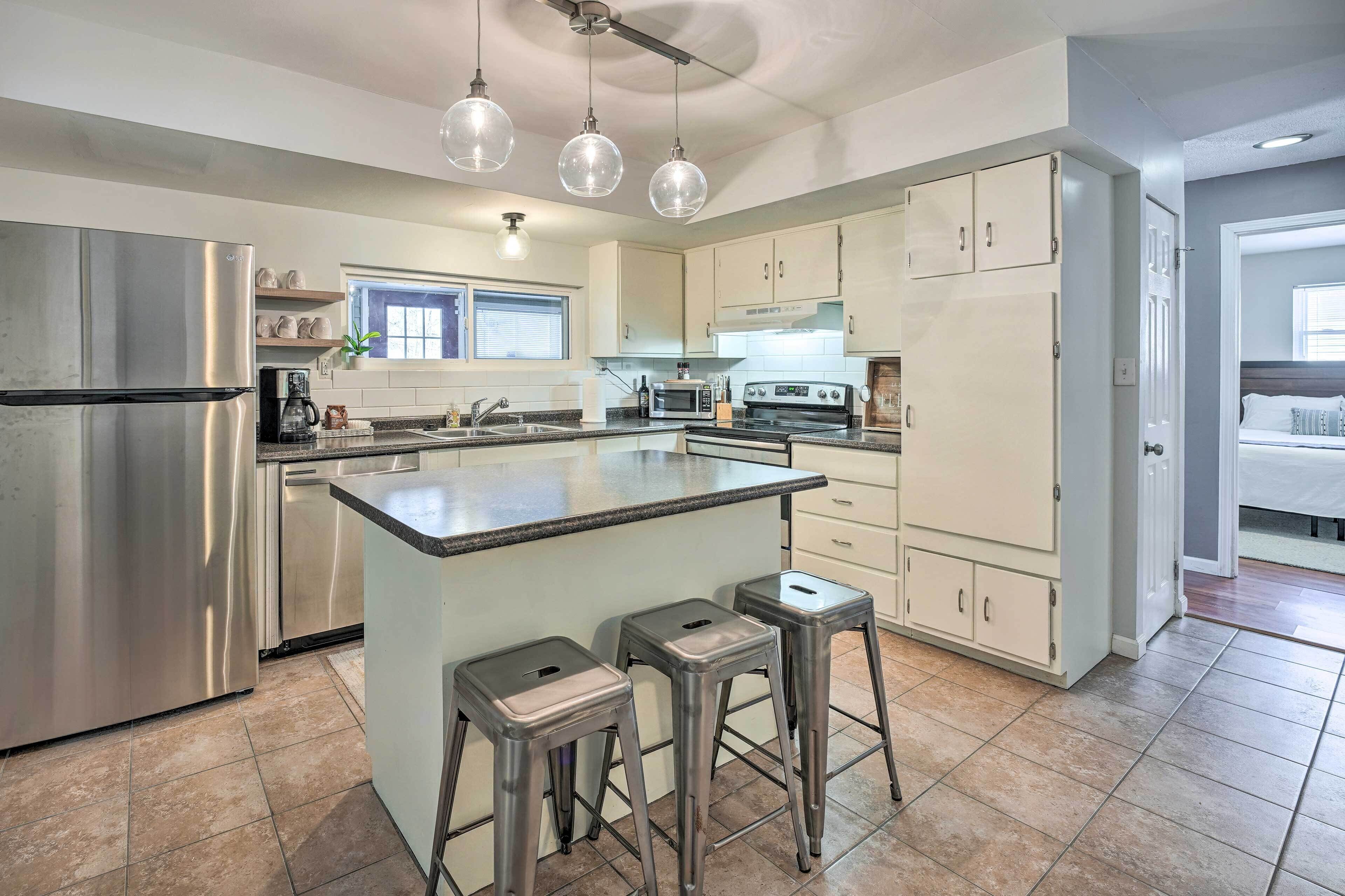A modern kitchen with stainless steel appliances, a central island with stools, and pendant lighting.