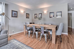 Un comedor con mesa de madera y sillas de metal, carteles enmarcados en la pared y una lámpara de pie.
