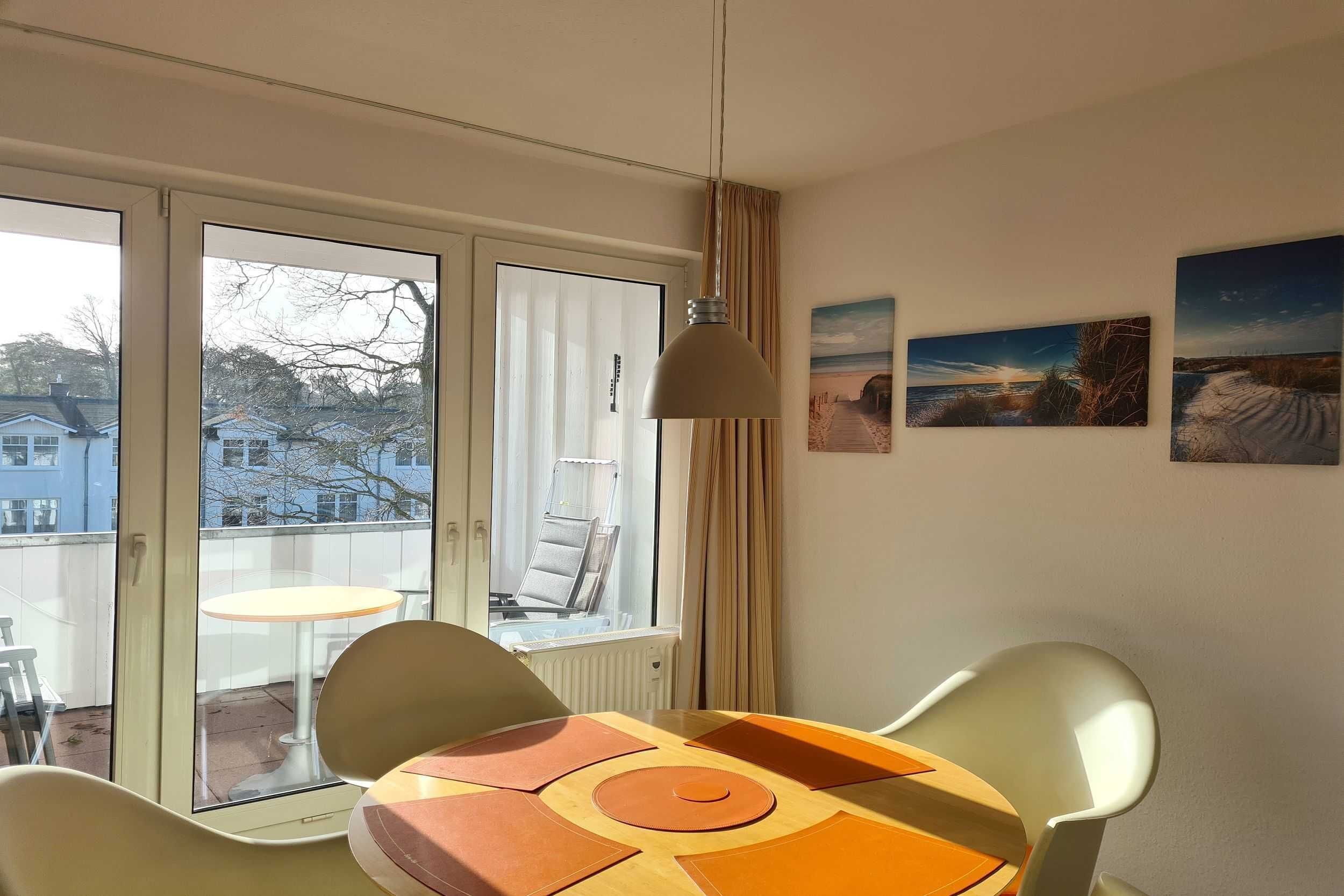 Une pièce avec une table et des chaises, une fenêtre avec des rideaux et trois tableaux accrochés au mur.