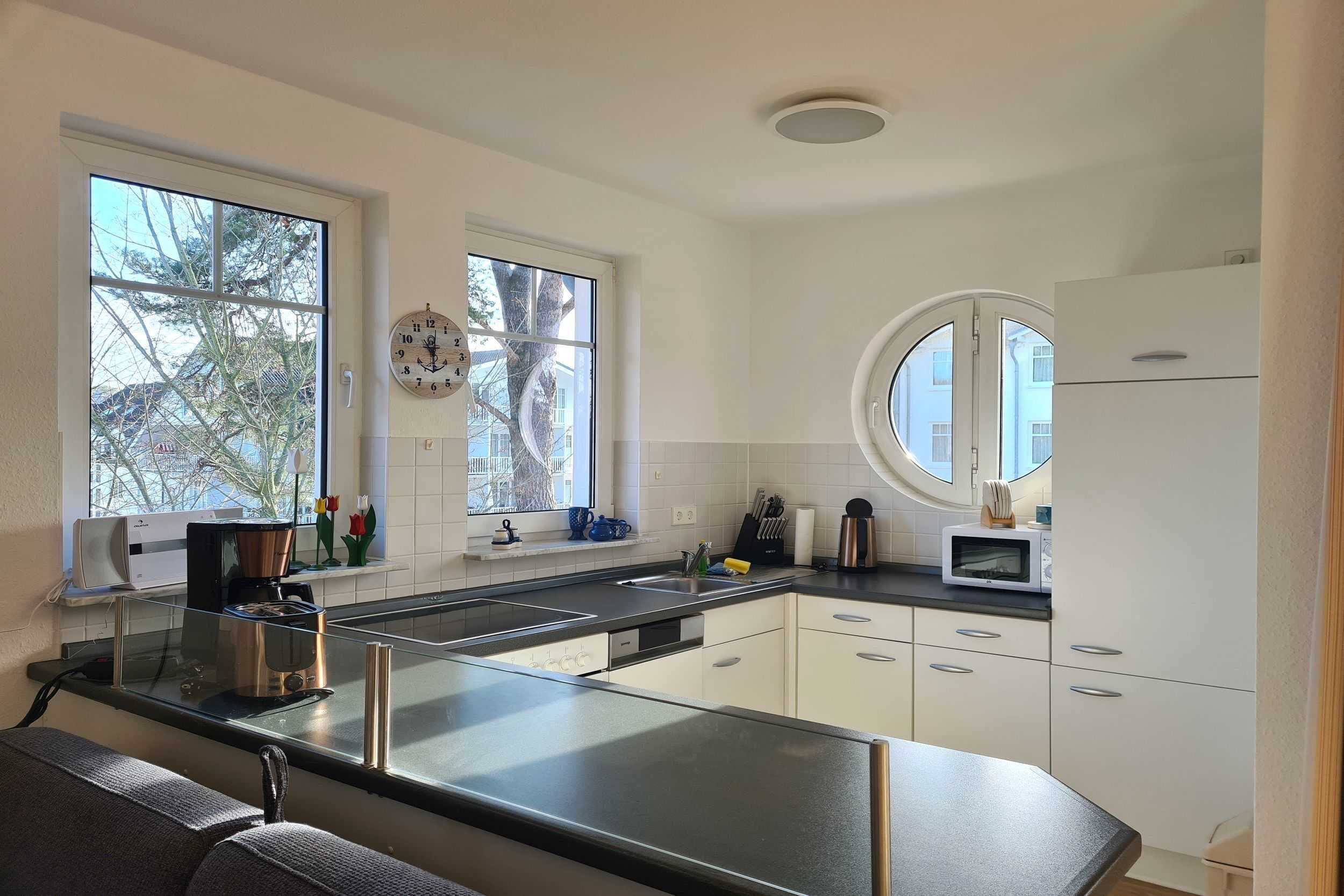 A modern kitchen with white cabinets, a black countertop, a coffee machine, and a microwave.
