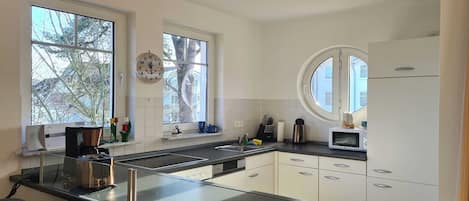 Una cocina moderna con armarios blancos, encimera negra, cafetera y microondas.