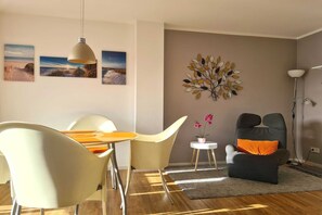 A modern living room with a dining area, featuring a sofa, chairs, a coffee table, and artwork on the walls. - Villa Stoertebeker Apartment 19 - Störtebeker 19: 60m², 2-raum, 4 Pers., Balkon, Wlan (Ostseebad Baabe)