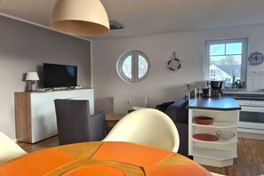 A modern living room with a TV, a round window, and a kitchen area with a kettle. - Villa Stoertebeker Apartment 19 - Störtebeker 19: 60m², 2-raum, 4 Pers., Balkon, Wlan (Ostseebad Baabe)