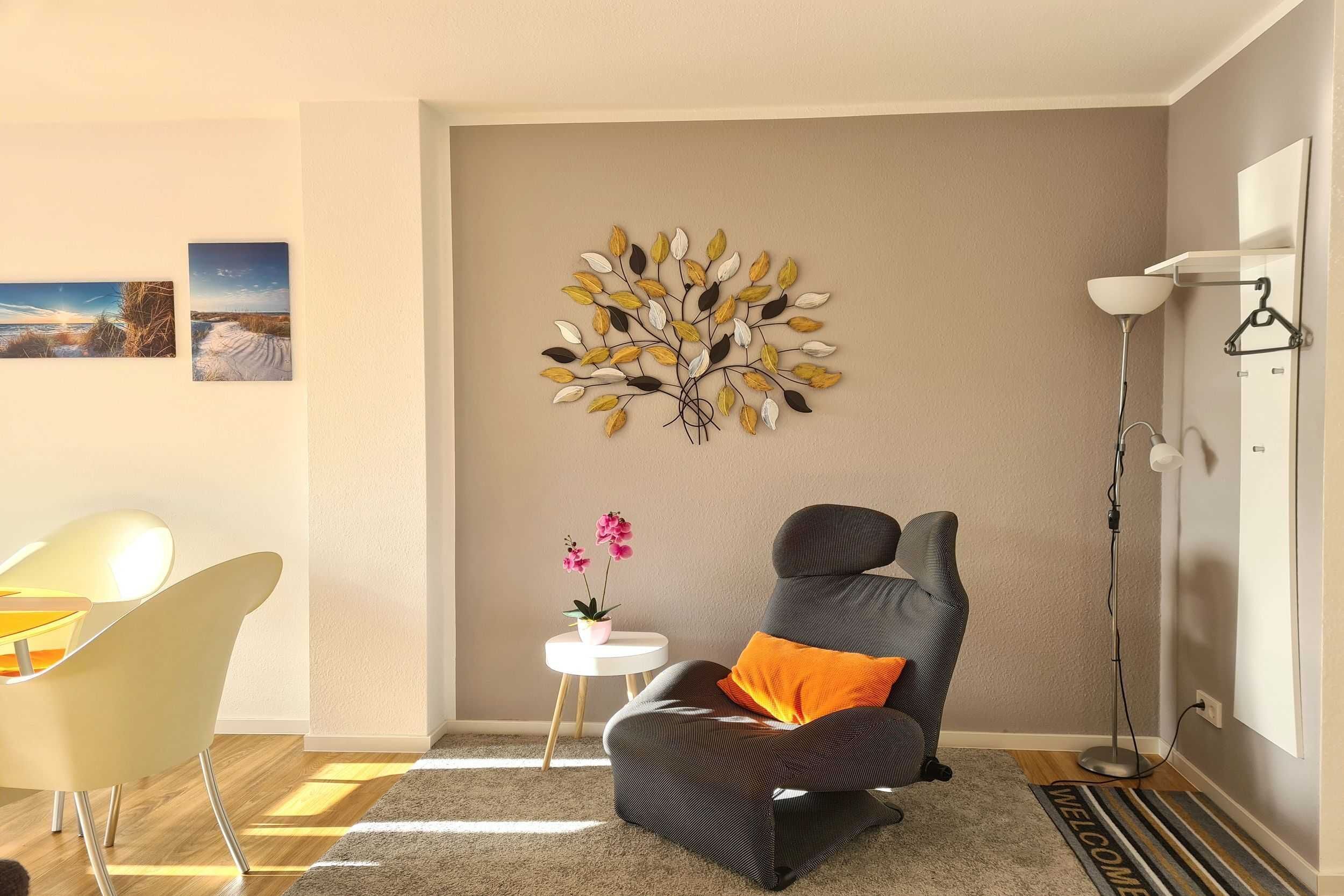 A modern living room with a gray sofa, a small white side table with a potted plant, a decorative wall piece, and a standing floor lamp.