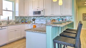 A kitchen with white cabinets, a microwave, a stove, and a sink. There is a window with a view of a hill. - Furnished Deck + Ocean Views: Surfside Beach Home (Surfside Beach)
