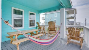 A turquoise house with a porch, wooden chairs, a hammock, and a wooden table. - Furnished Deck + Ocean Views: Surfside Beach Home (Surfside Beach)