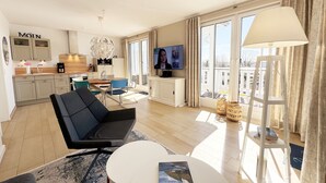Ein modernes Wohnzimmer mit einer Couch, einem Couchtisch und einem Fernseher. Es gibt eine Küchenzeile mit Schränken und einem Esstisch.