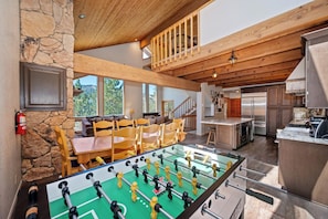A spacious living area with a foosball table, a kitchen with modern appliances, and a stone wall.