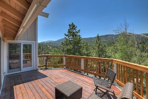 A wooden deck with outdoor furniture, a glass door entrance, and a view of a forested mountain range. - Breathtaking Ski Slope Views in Upper Moonridge! HOT TUB! Pet friendly! Arcade Games! Foosball! (Big Bear Lake)