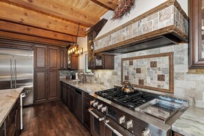 Una cocina moderna con un refrigerador de acero inoxidable, estufa a gas, gabinetes de madera y un salpicadero de piedra.